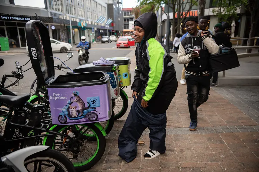 Through rain and shine, Pitcher works. Expecting cooler weather, she puts on a pair of warmer overpants during her Saturday afternoon shift outside Cavendish Square in Claremont. Picture: David Harrison/@GroundUp News Through rain and shine, Pitcher works. Expecting cooler weather, she puts on a pair of warmer overpants during her Saturday afternoon shift outside Cavendish Square in Claremont. Picture: David Harrison/@GroundUp News