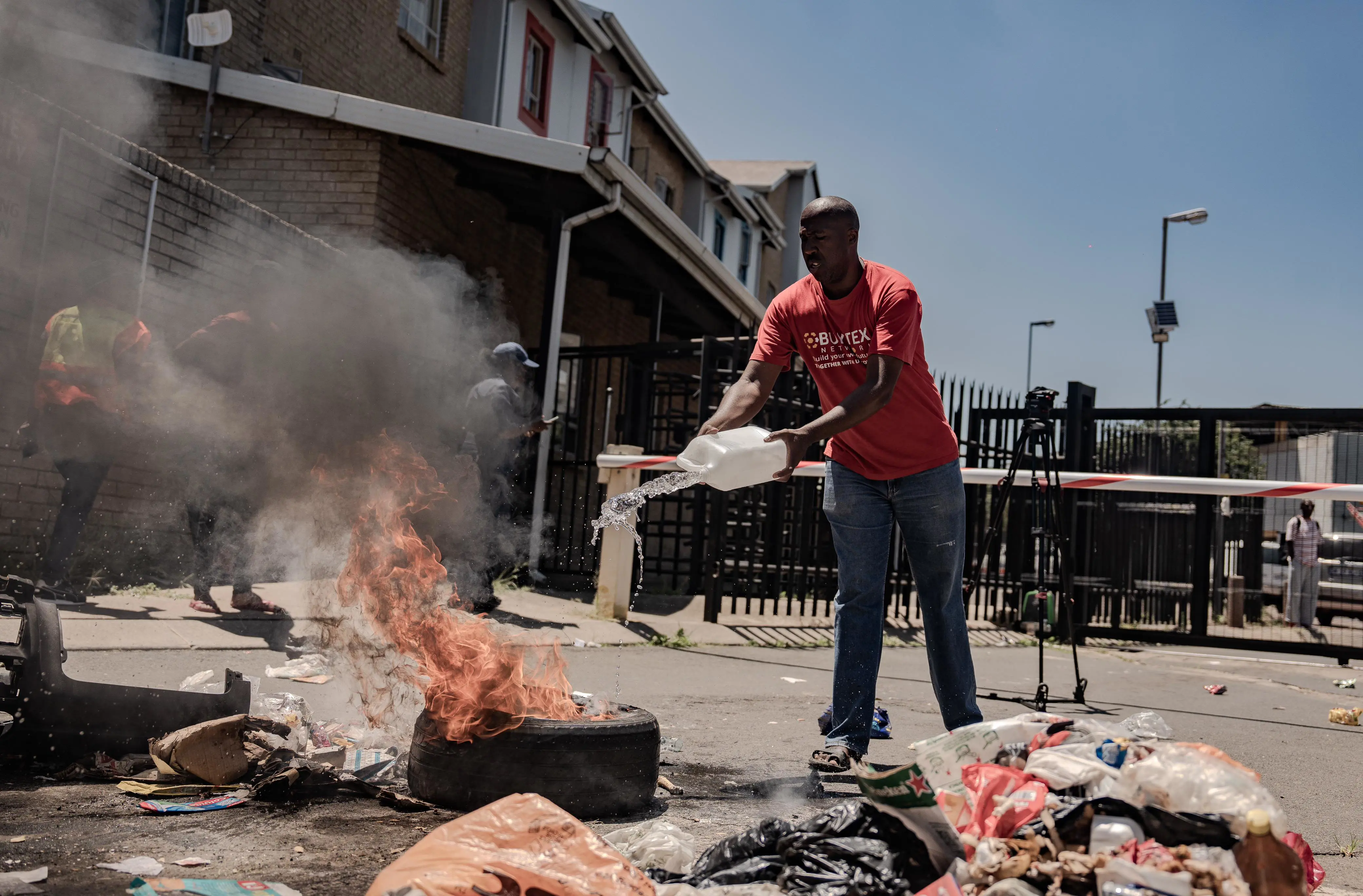 A Kliptown Square resident exinguishes a fire during a protest against City Power cutting illegal electricity connections at the complex on 29 January 2025. Picture: Sphamandla Dlamini/EWN A Kliptown Square resident exinguishes a fire during a protest against City Power cutting illegal electricity connections at the complex on 29 January 2025. Picture: Sphamandla Dlamini/EWN